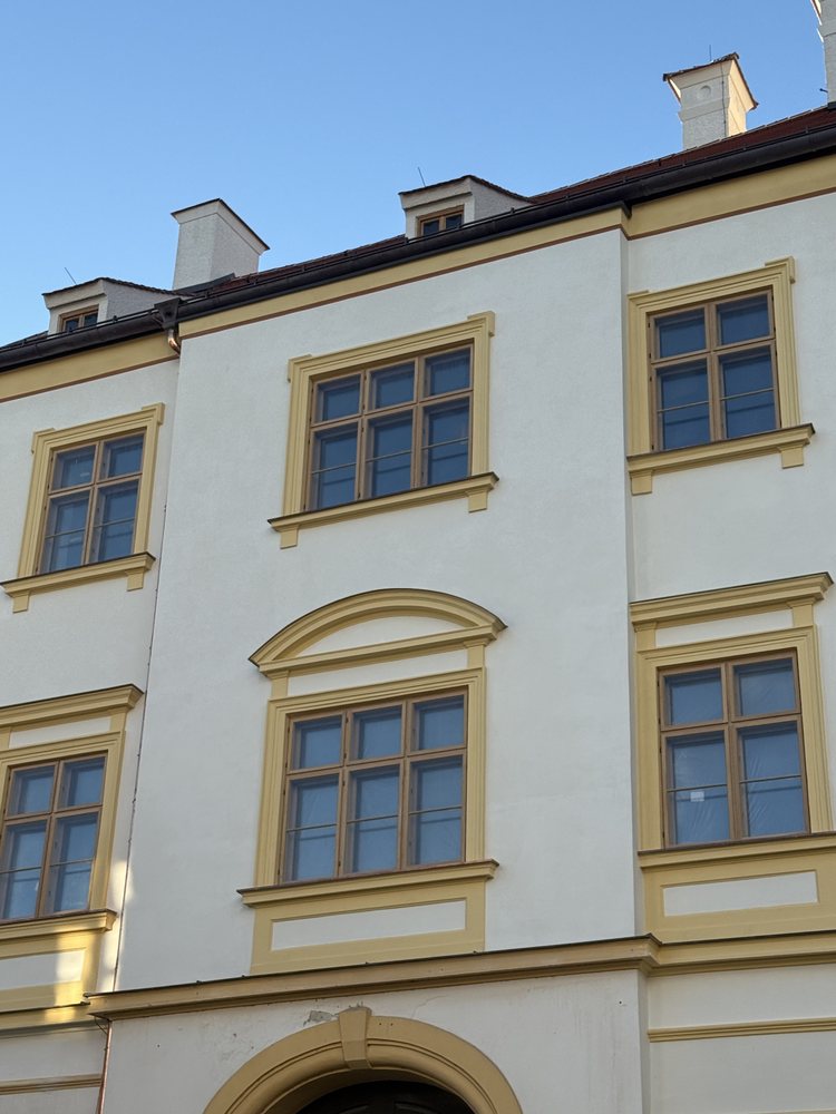 Hell verputzte Fassade mit ockerfarbenen Fenstergewänden und Gesimsen