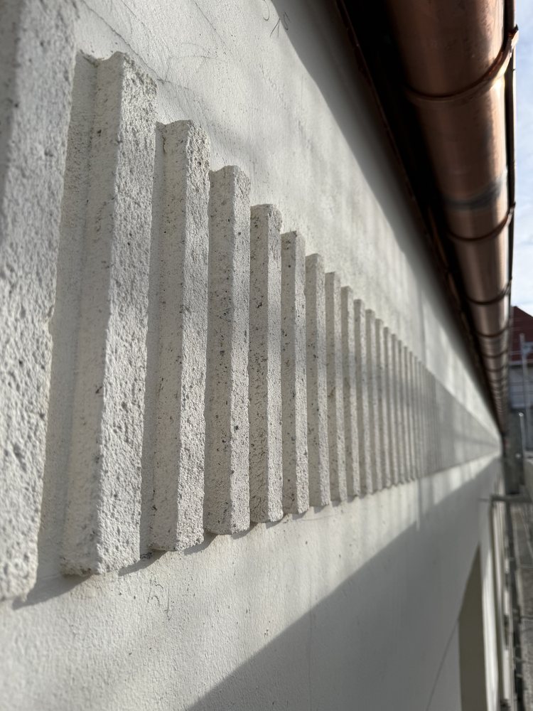 Gesims mit Zahnschnitt aus Kalkputz an einer hellen Fassade im Streiflicht